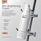 A 15ml bottle of Rhama Skin +16 Skin Brightening Cream is shown hanging from a chrome stand against a light gray background. The bottle is white with black and orange text.